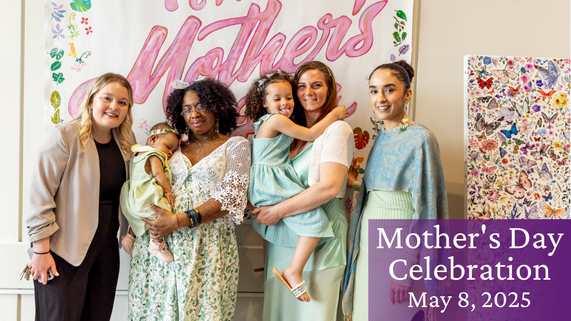 Four women, two holding children, in front of a Mother's Day banner