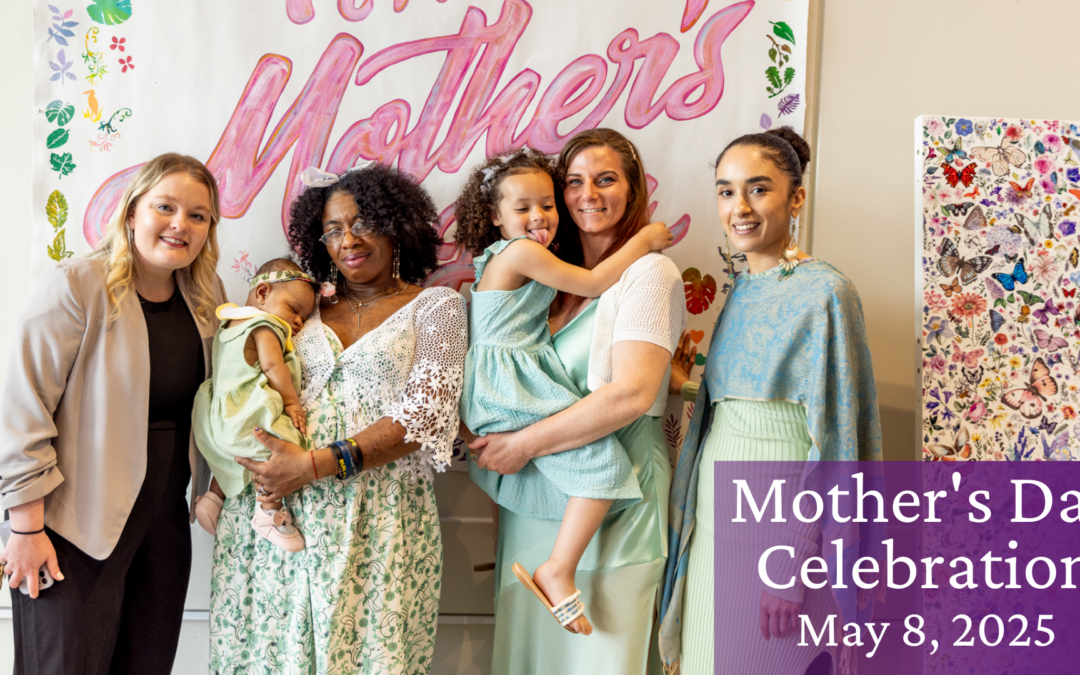 Four women, two holding children, in front of a Mother's Day banner